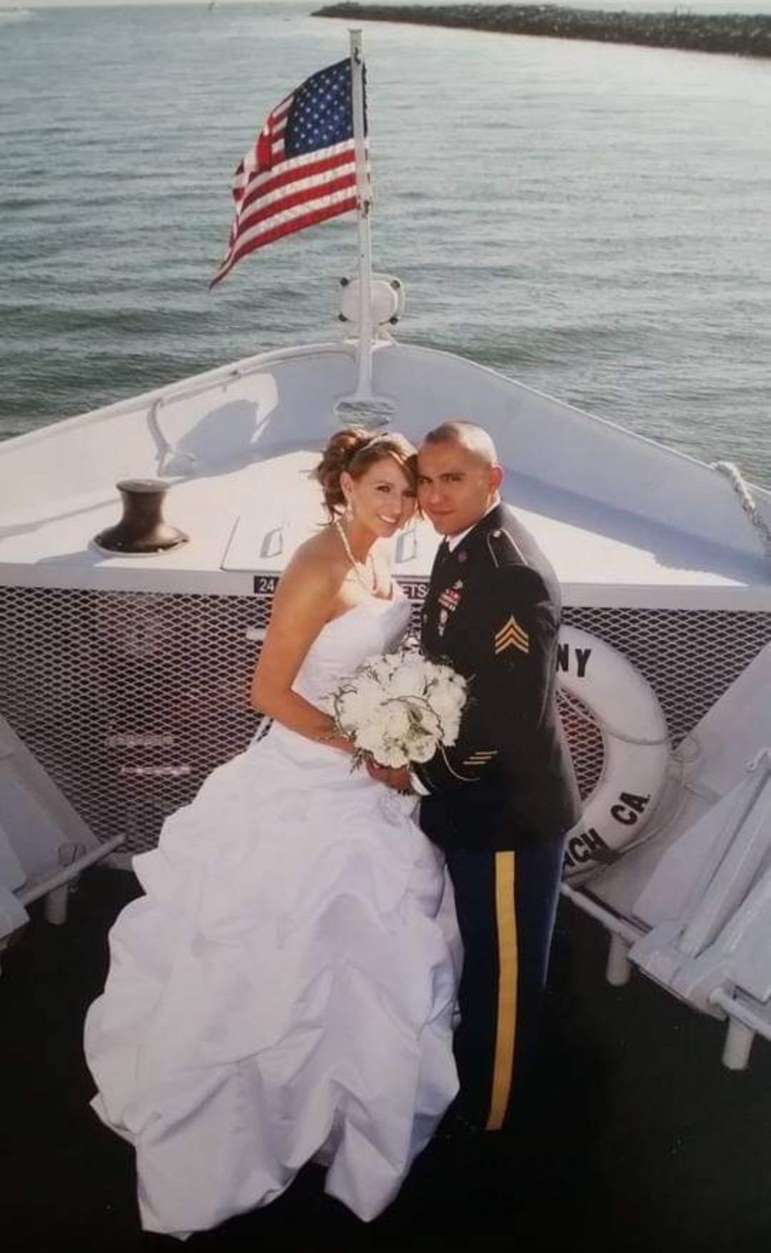A bride and groom pose on a boat with an american flag in the background