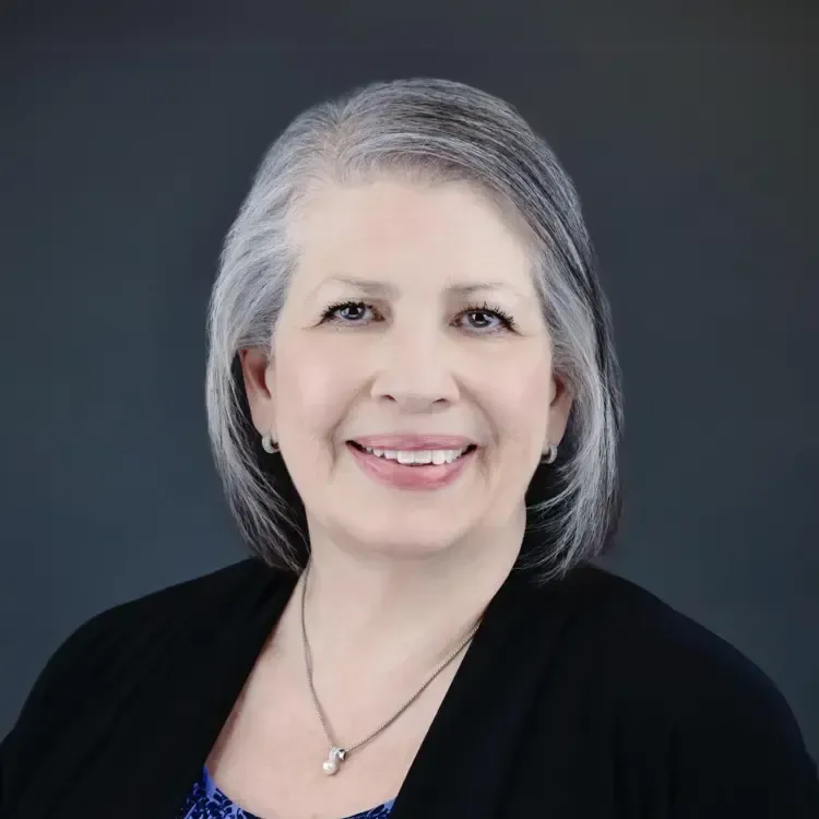 A woman with gray hair and a necklace is smiling for the camera.