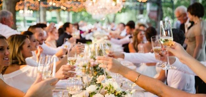 A group of people are sitting at a long table toasting with champagne glasses.