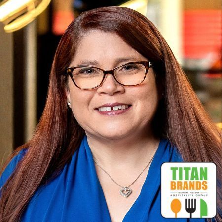 Woman with glasses smiling, wearing blue shirt, Titan Brands logo in corner.