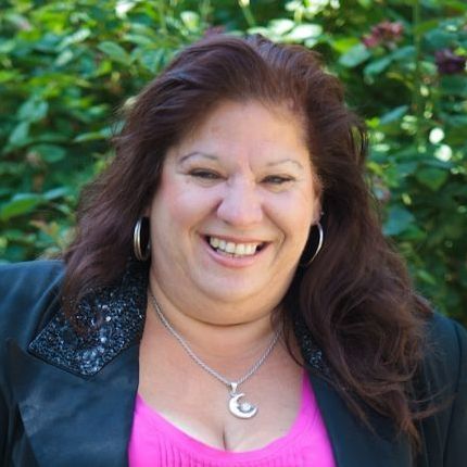 A woman in a purple suit is smiling in front of a green landscape background