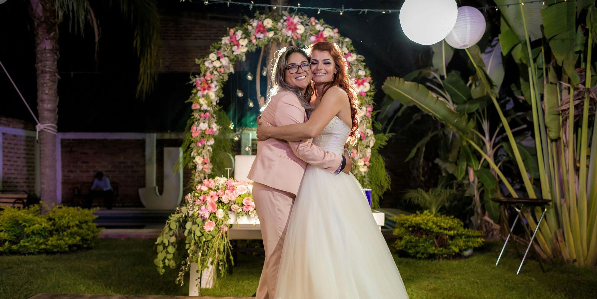 A bride and groom are posing for a picture in front of a floral arch.