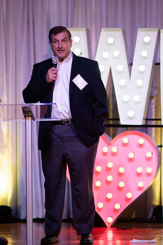 A man in a suit is standing at a podium holding a microphone.