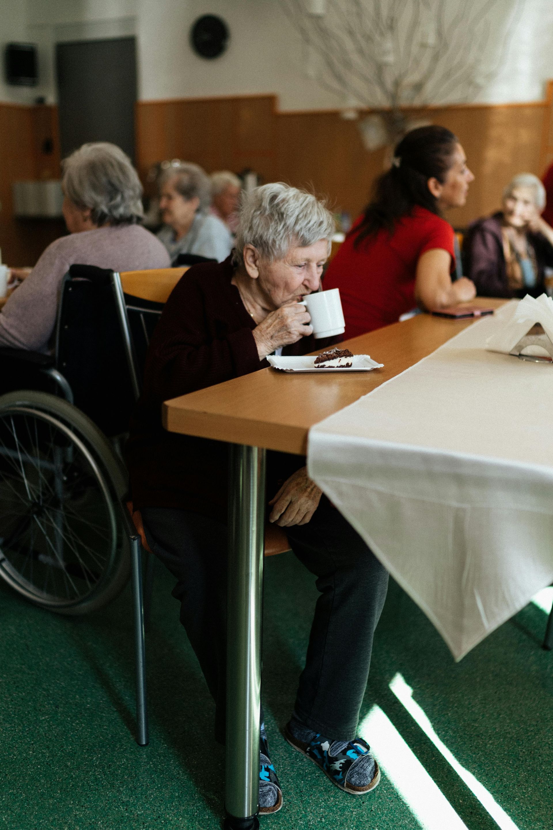 A woman in a wheelchair is sitting at a table drinking a cup of coffee.