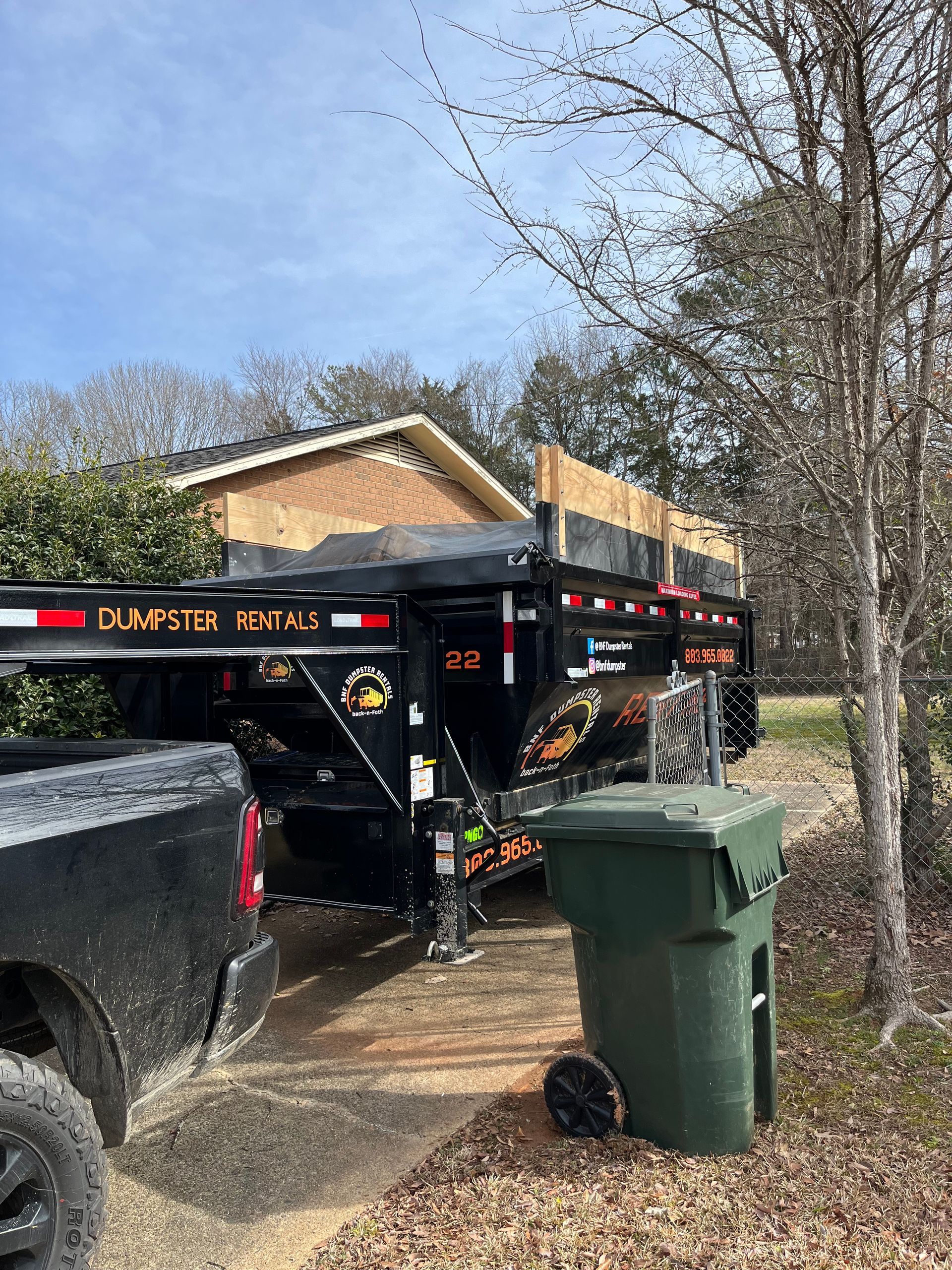 a dumpster is parked next to a trash can in front of a house .
