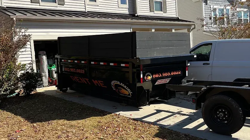 a dumpster is parked in front of a house next to a truck .