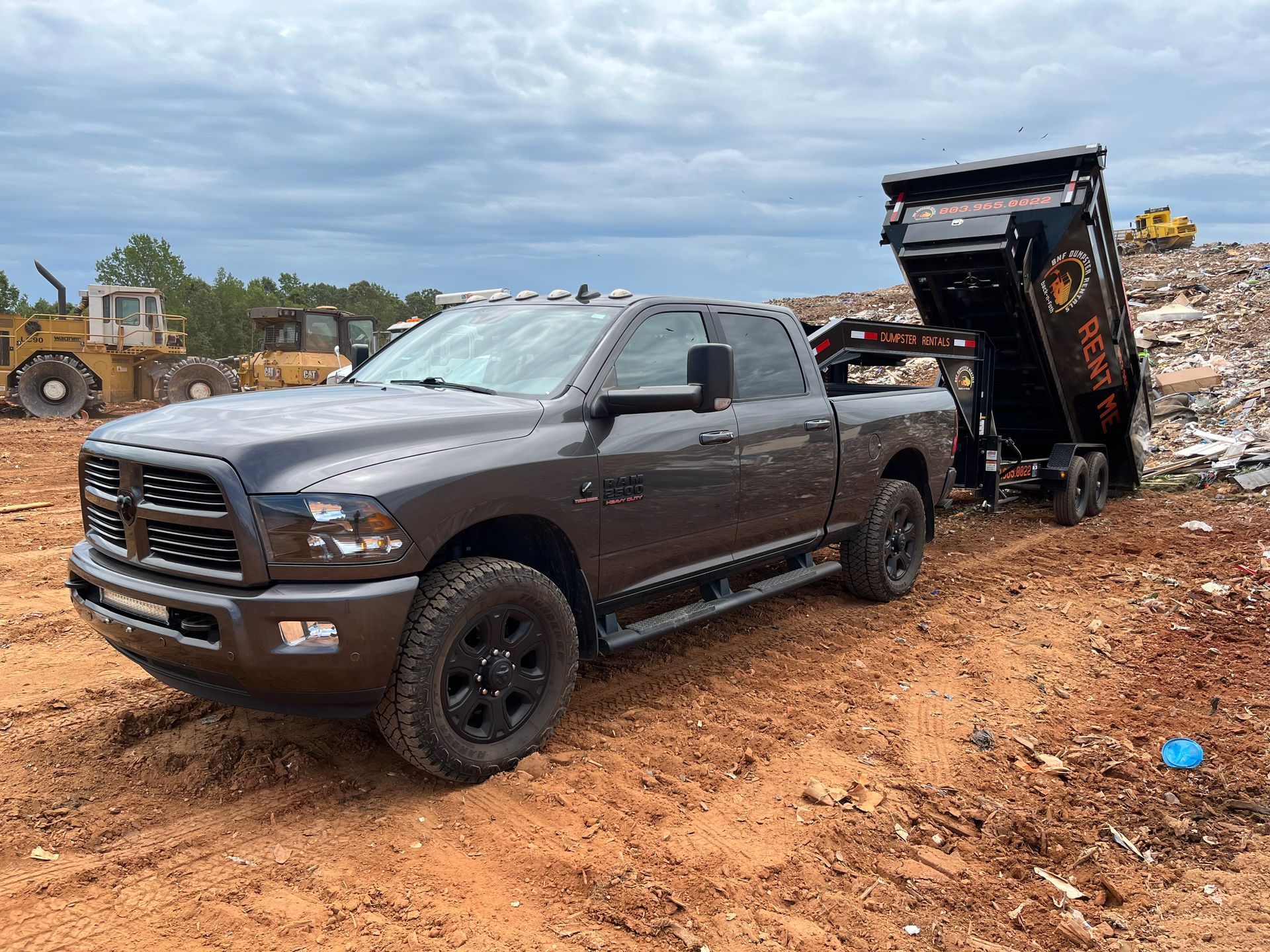 a gray ram truck is parked in the dirt next to a dumpster .