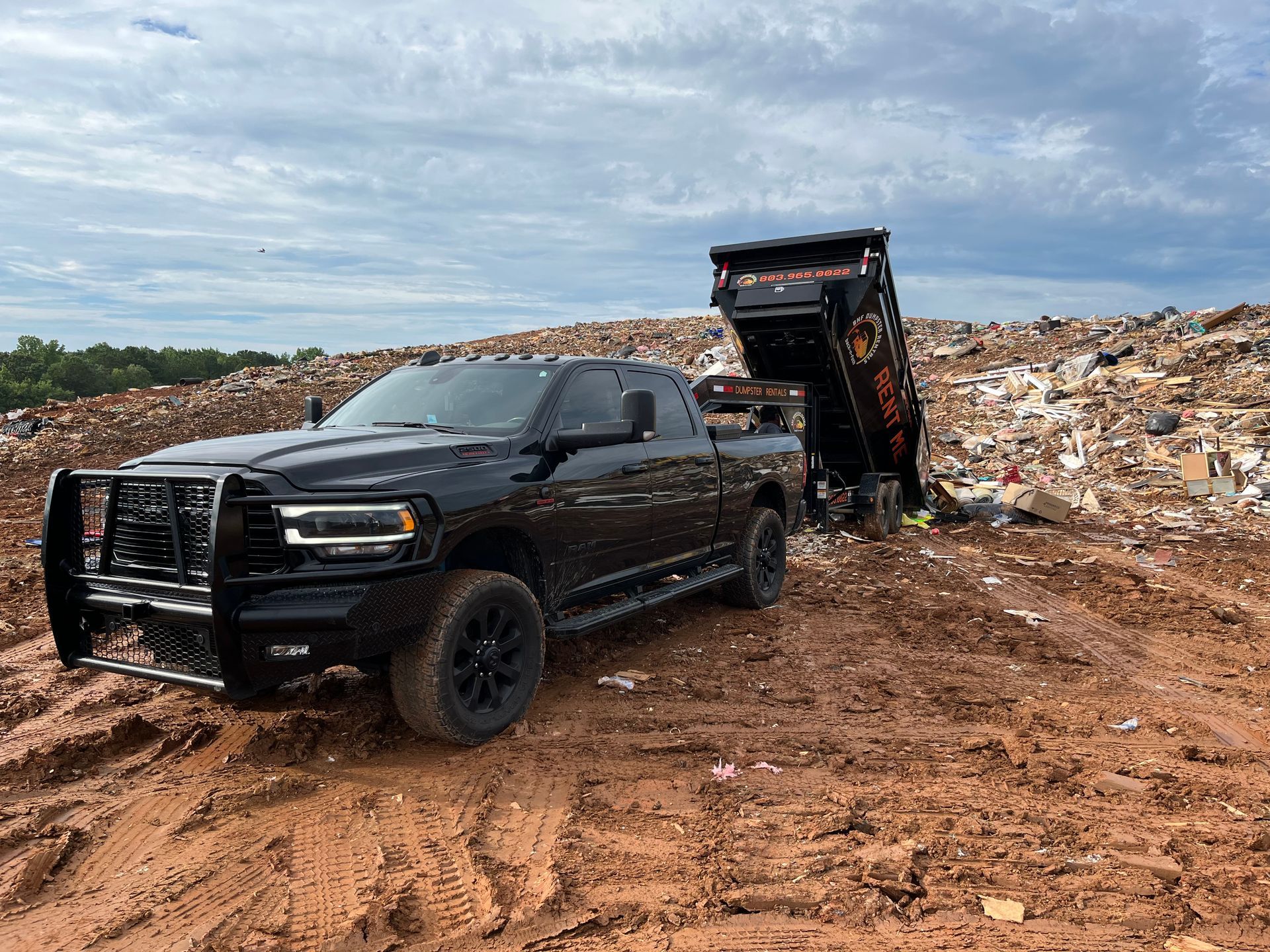 a black truck is parked in a dirt field next to a dumpster .