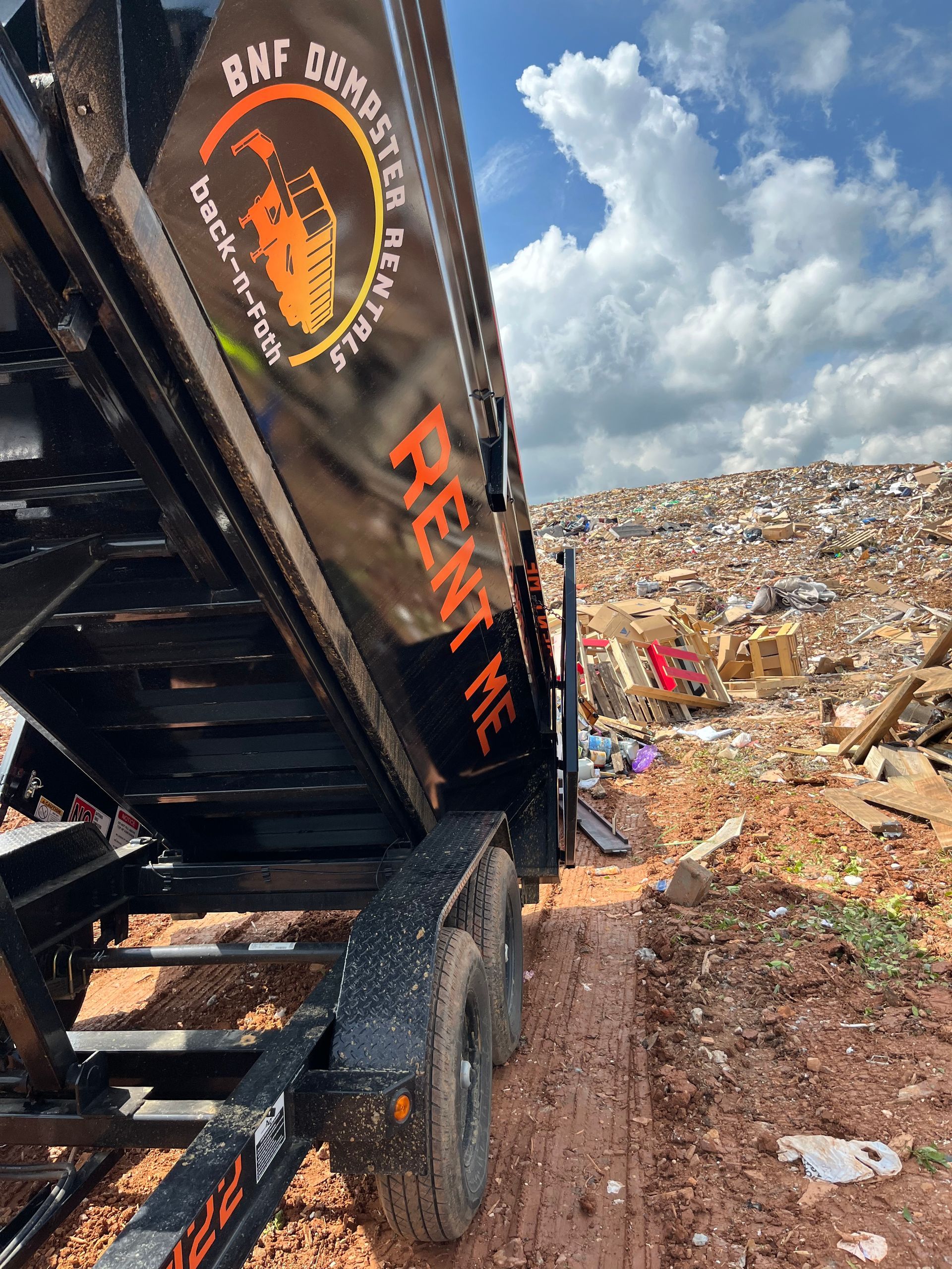 a metal dumpster throwing trash in a garbage field