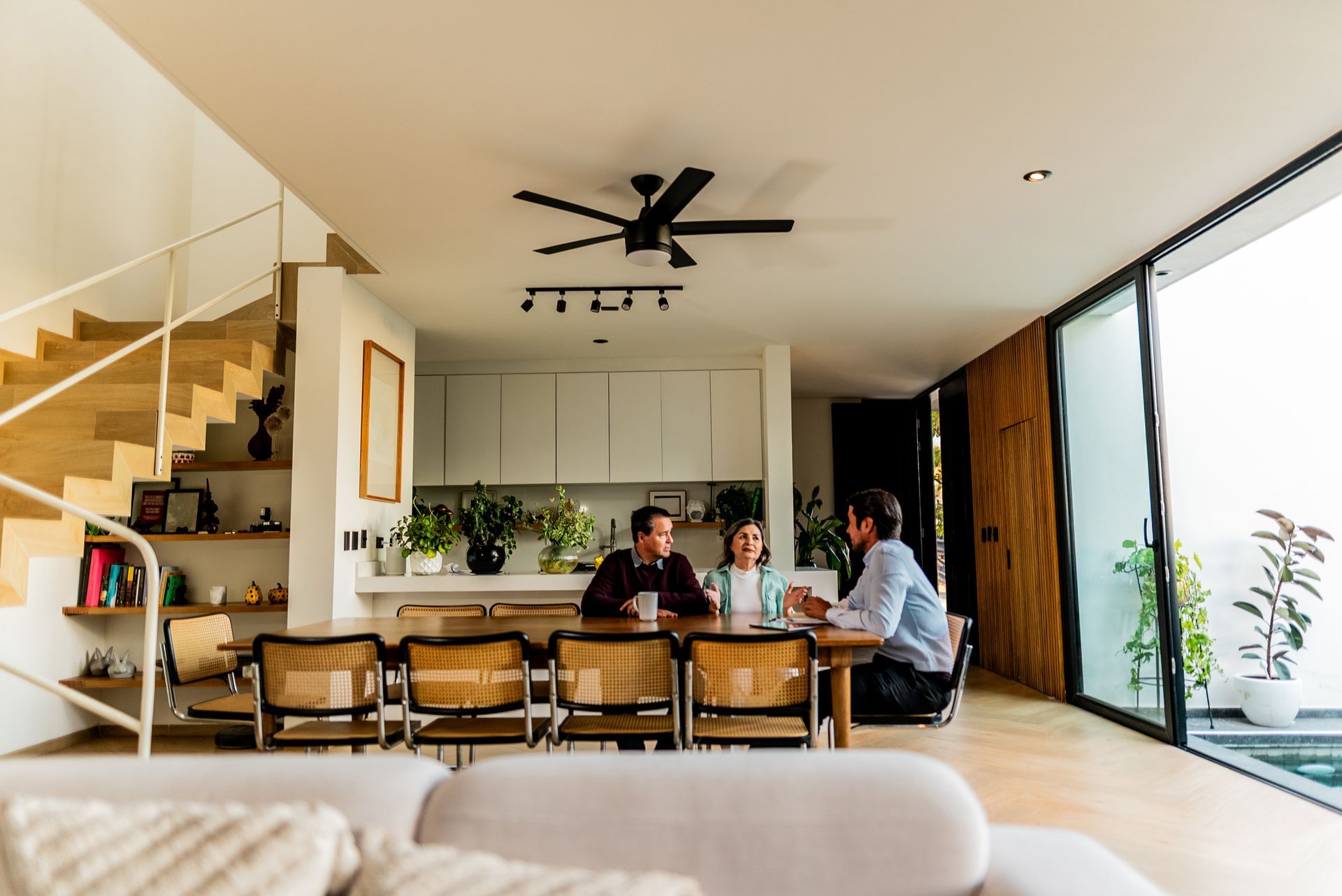 People at a dining table, having a discussion in a modern, well-lit home.