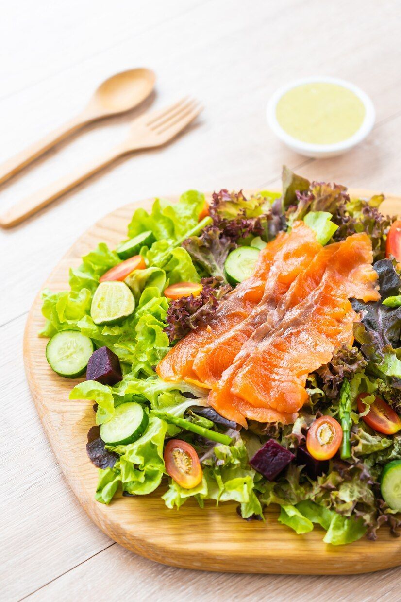 A salad with smoked salmon and vegetables on a wooden cutting board.