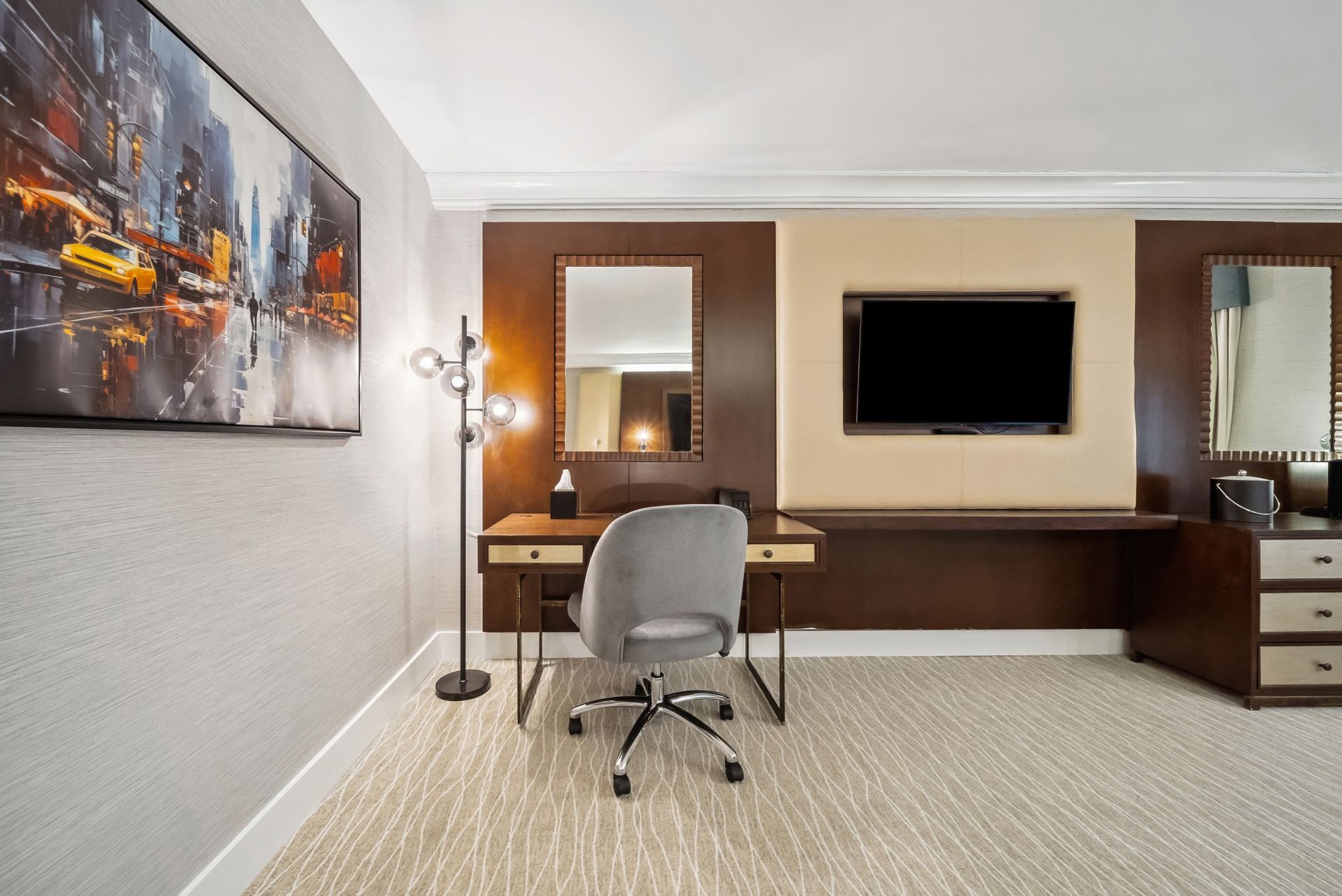 A hotel room with a desk , chair , television and mirror.