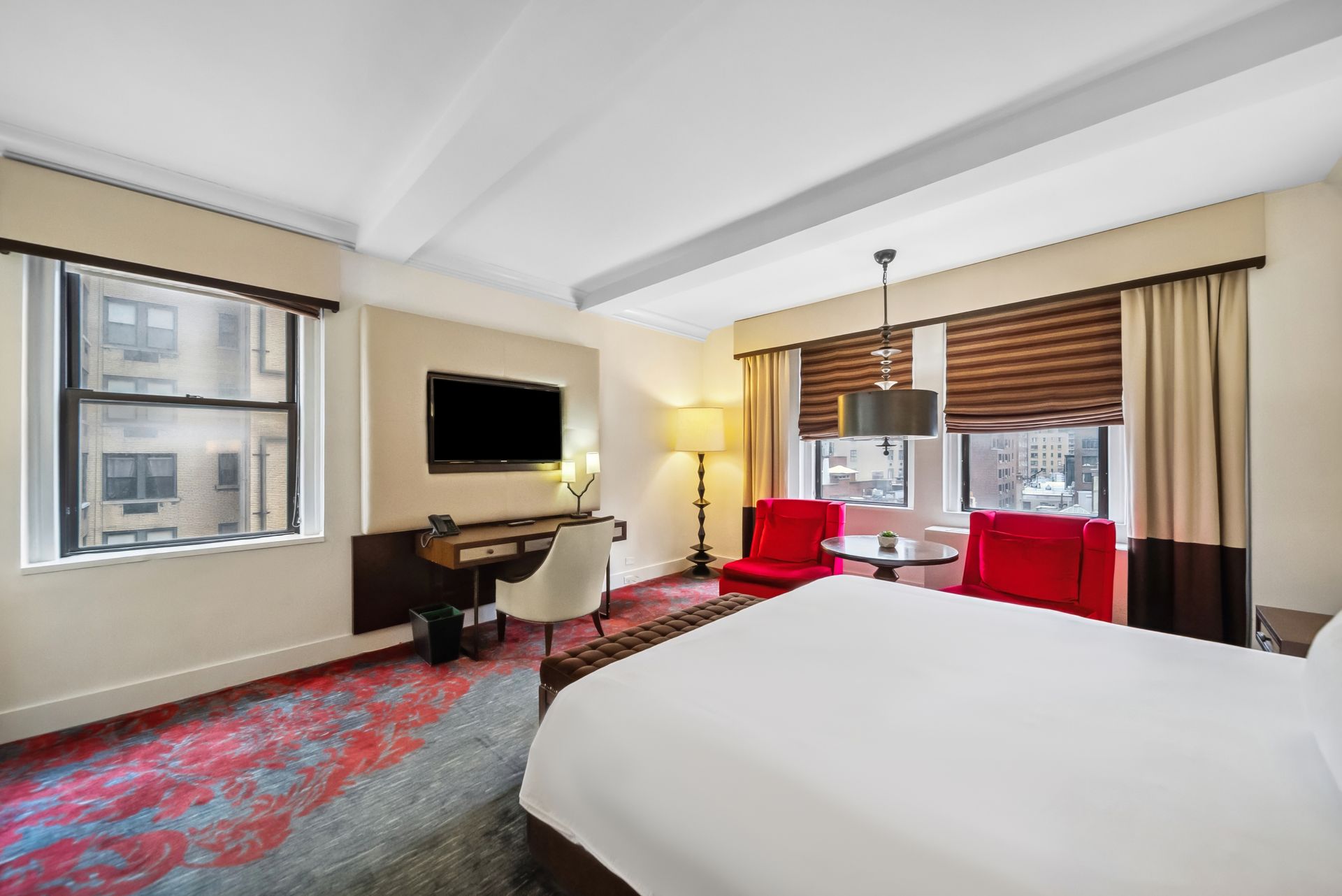 A hotel room with a king size bed , chairs , desk and television.