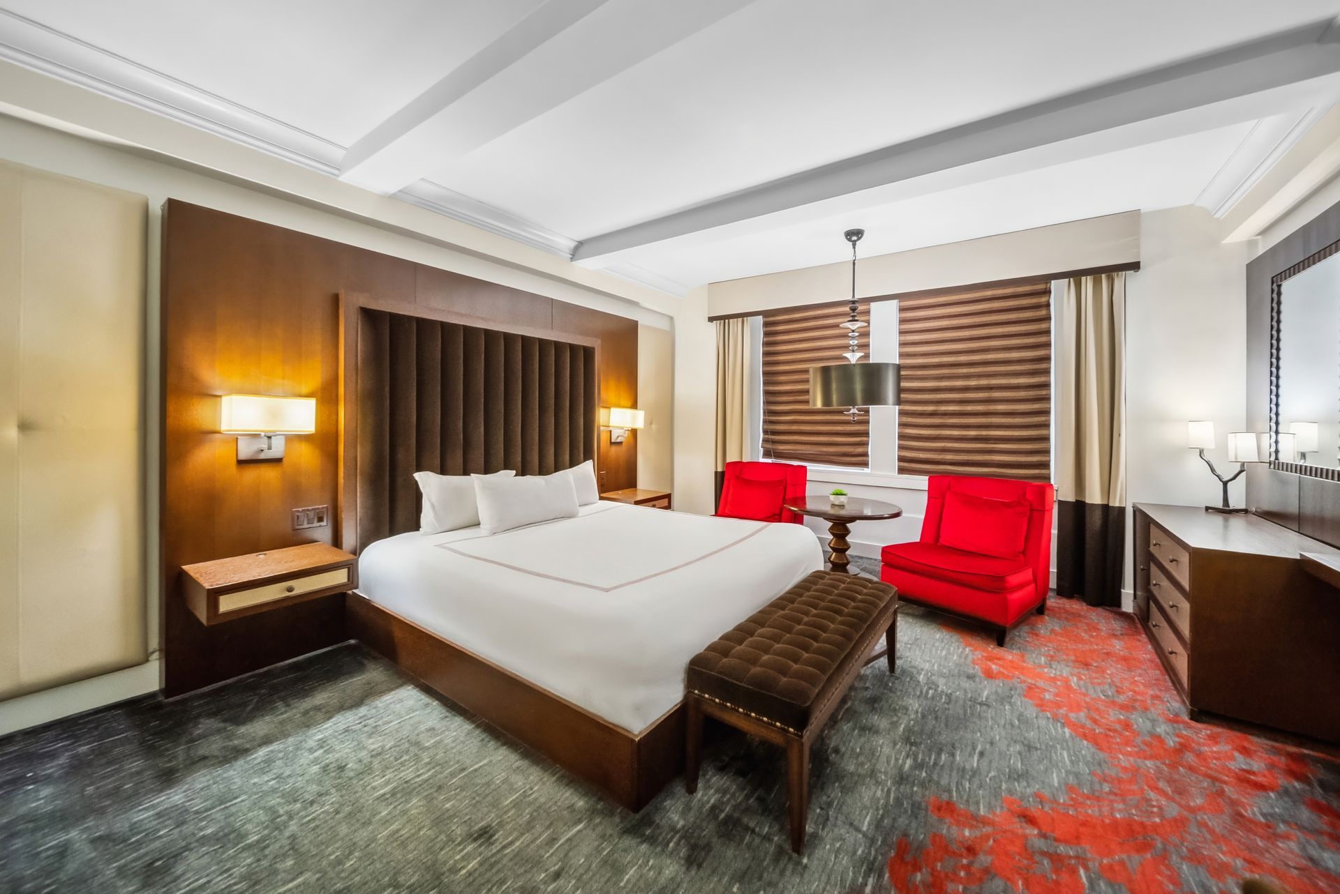 A hotel room with a king size bed and red chairs.