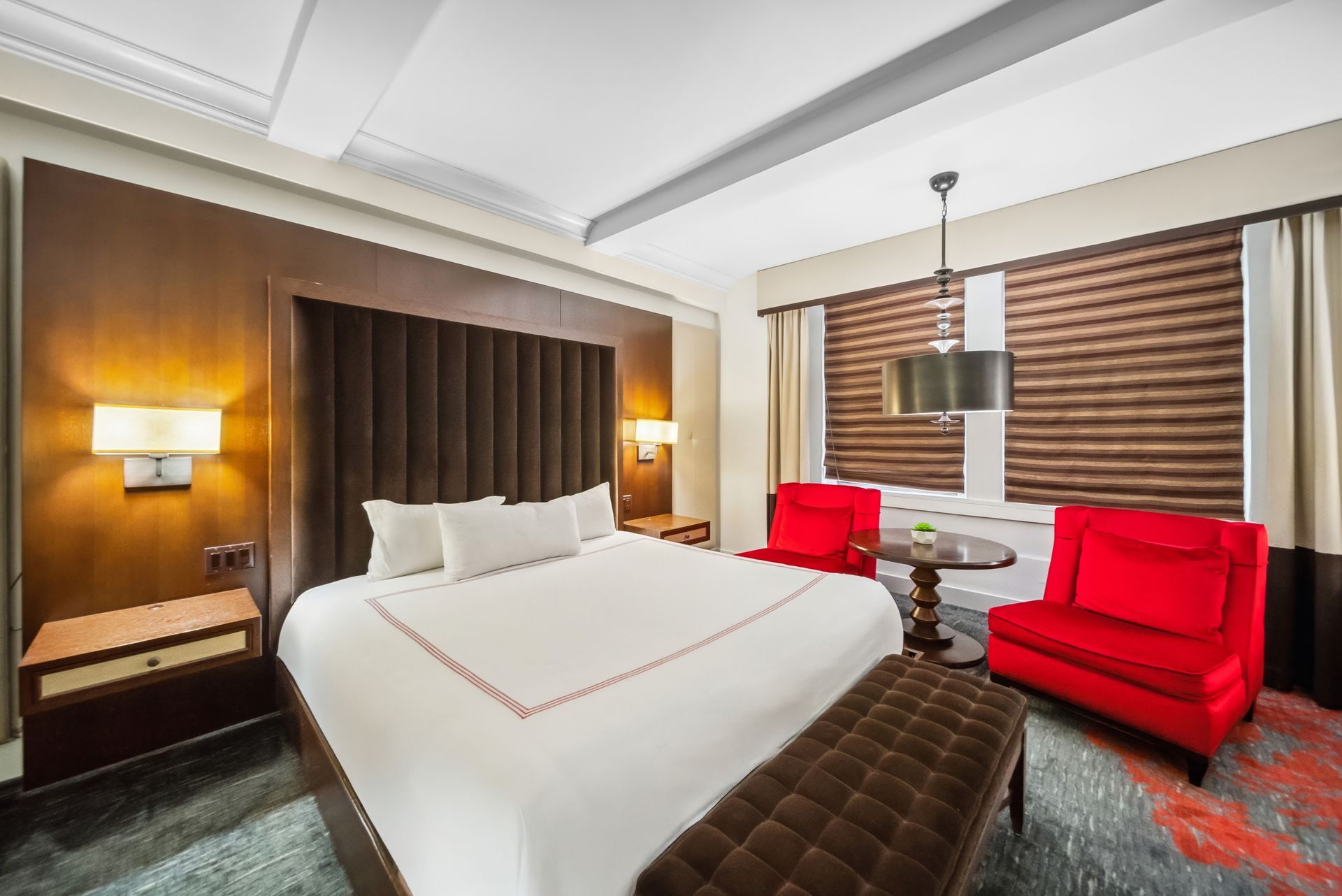 A hotel room with a king size bed and red chairs.