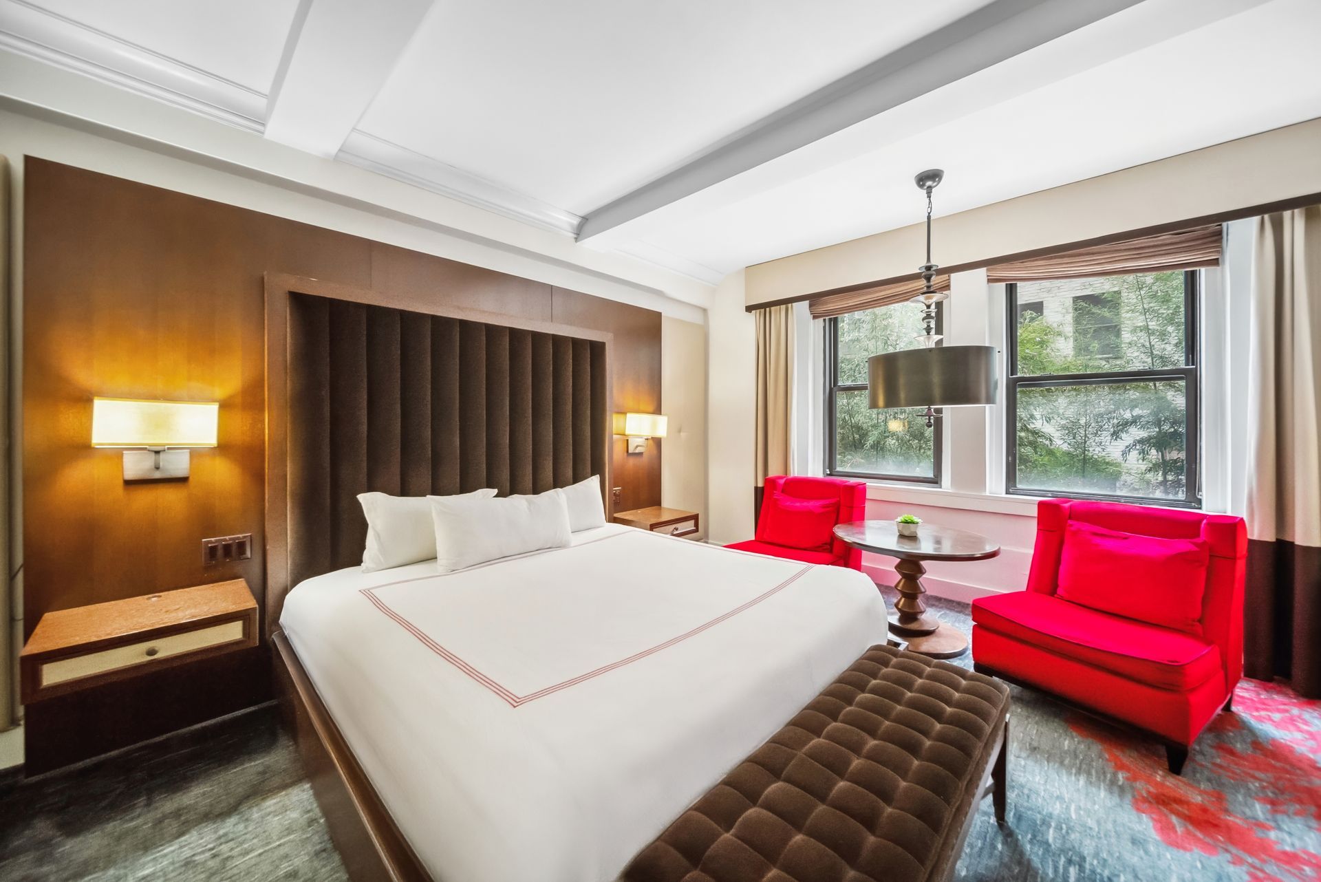 A hotel room with a king size bed and two red chairs.