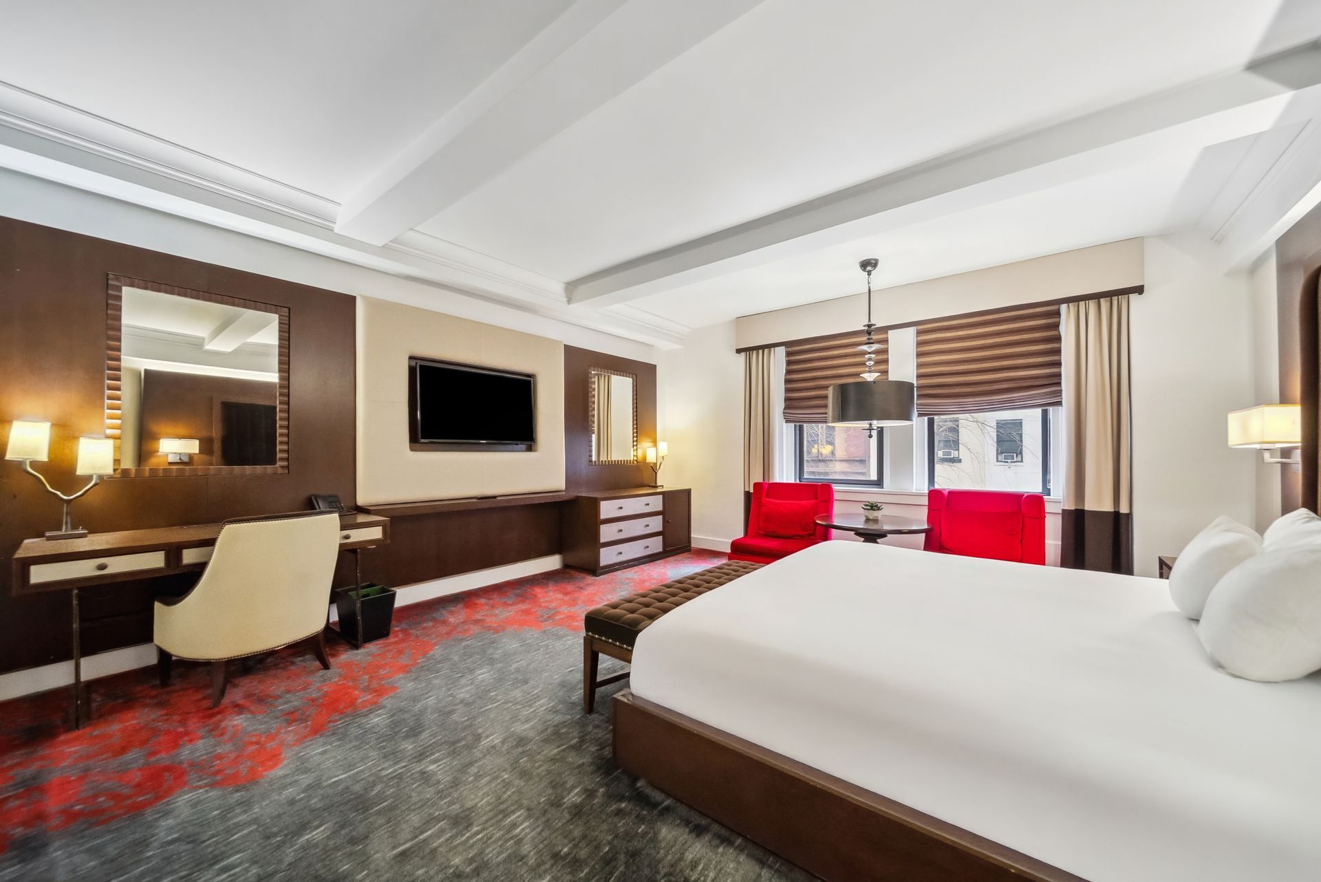 A hotel room with a king size bed , chairs , desk and television.