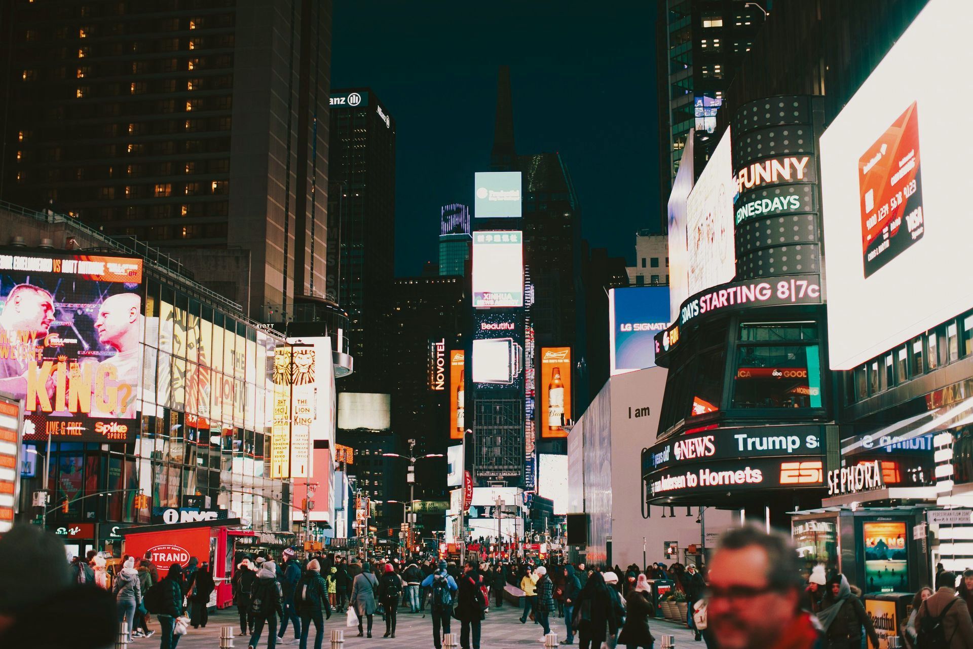 A crowd of people are walking down a busy city street at night.