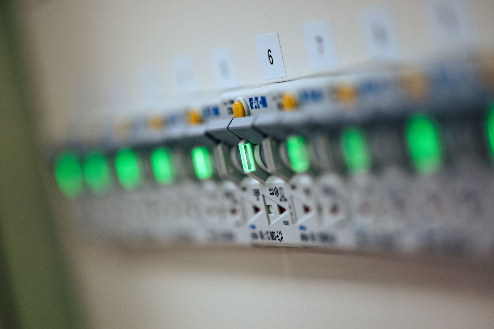 En rekke elektriske sikringsbrytere med knallgrønne statusindikatorer som lyser på et kontrollpanel.