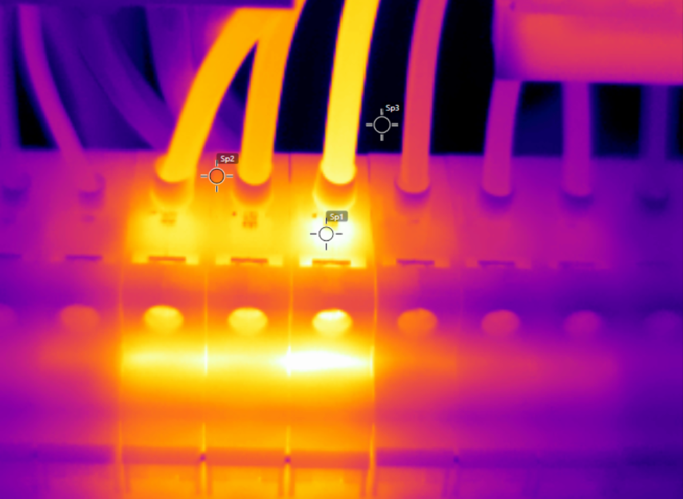 Termisk bilde av et elektrisk panel som viser et varmt punkt ved en terminaltilkobling med klare gulhvite varmesignaturer.