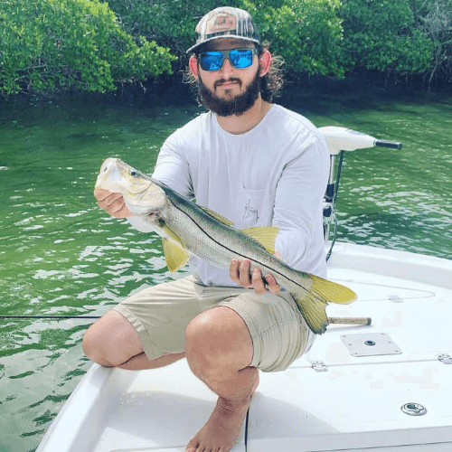 A man is kneeling on a boat holding a large fish.
