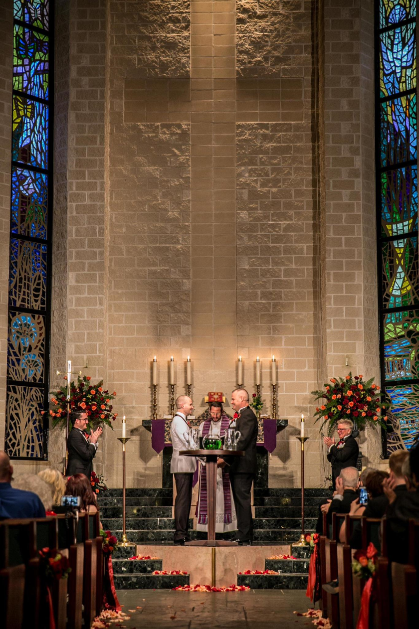 Simple wedding setup with floral arrangements and two grooms with a minister