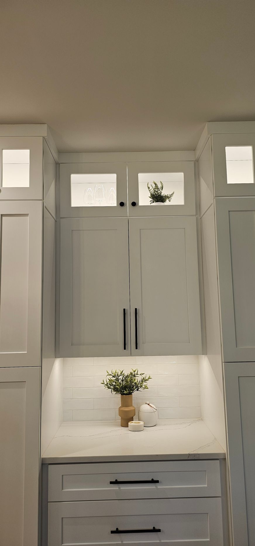 White kitchen cabinets with under-cabinet lighting, a countertop display of a vase of flowers.