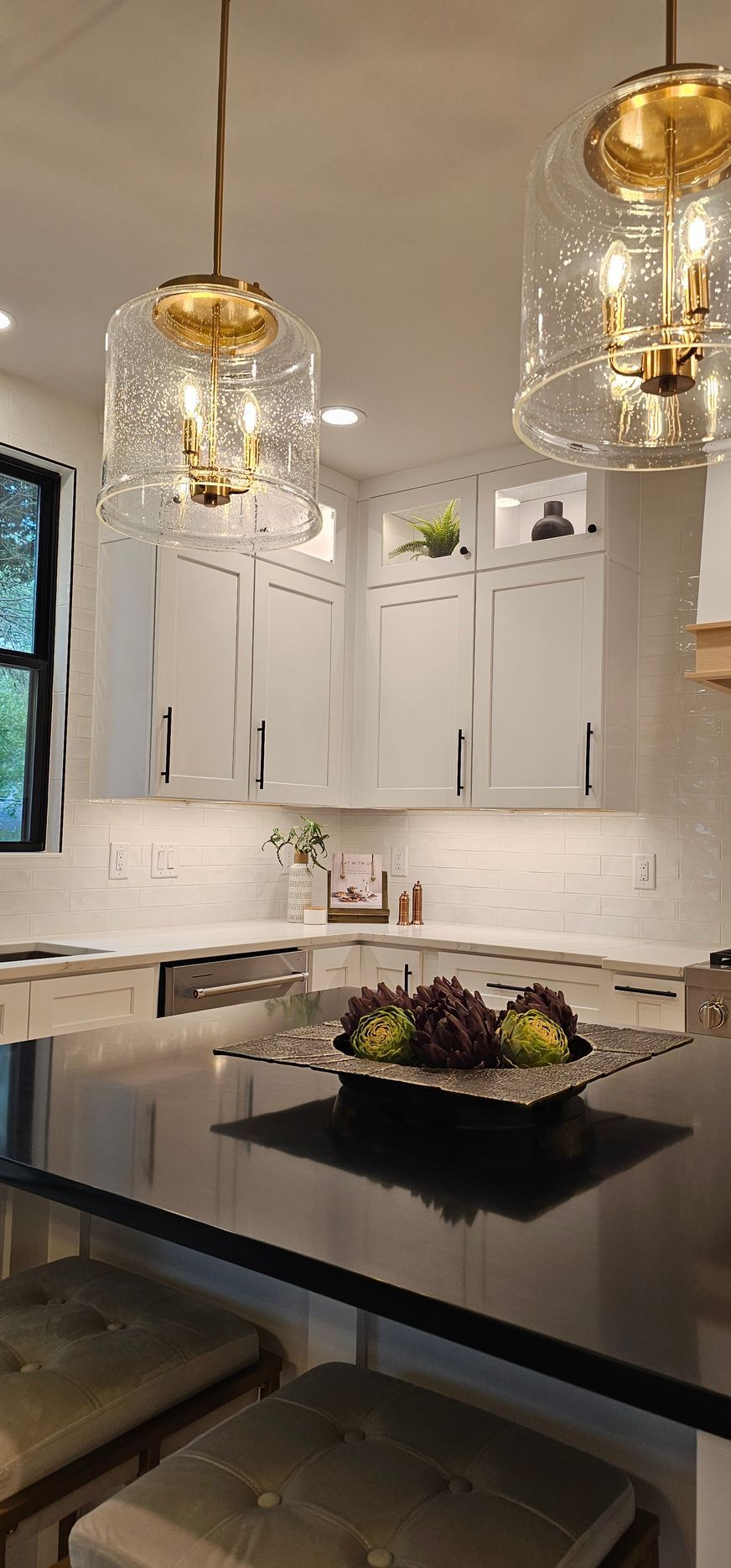 A modern kitchen with white cabinets, black countertops, and pendant lights. A bowl of fruit sits on the island.