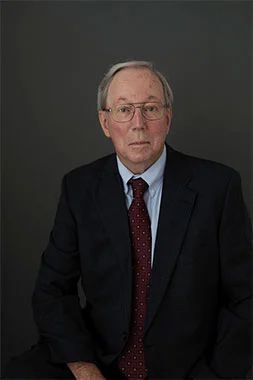 A man in a suit and tie is sitting down and looking at the camera.