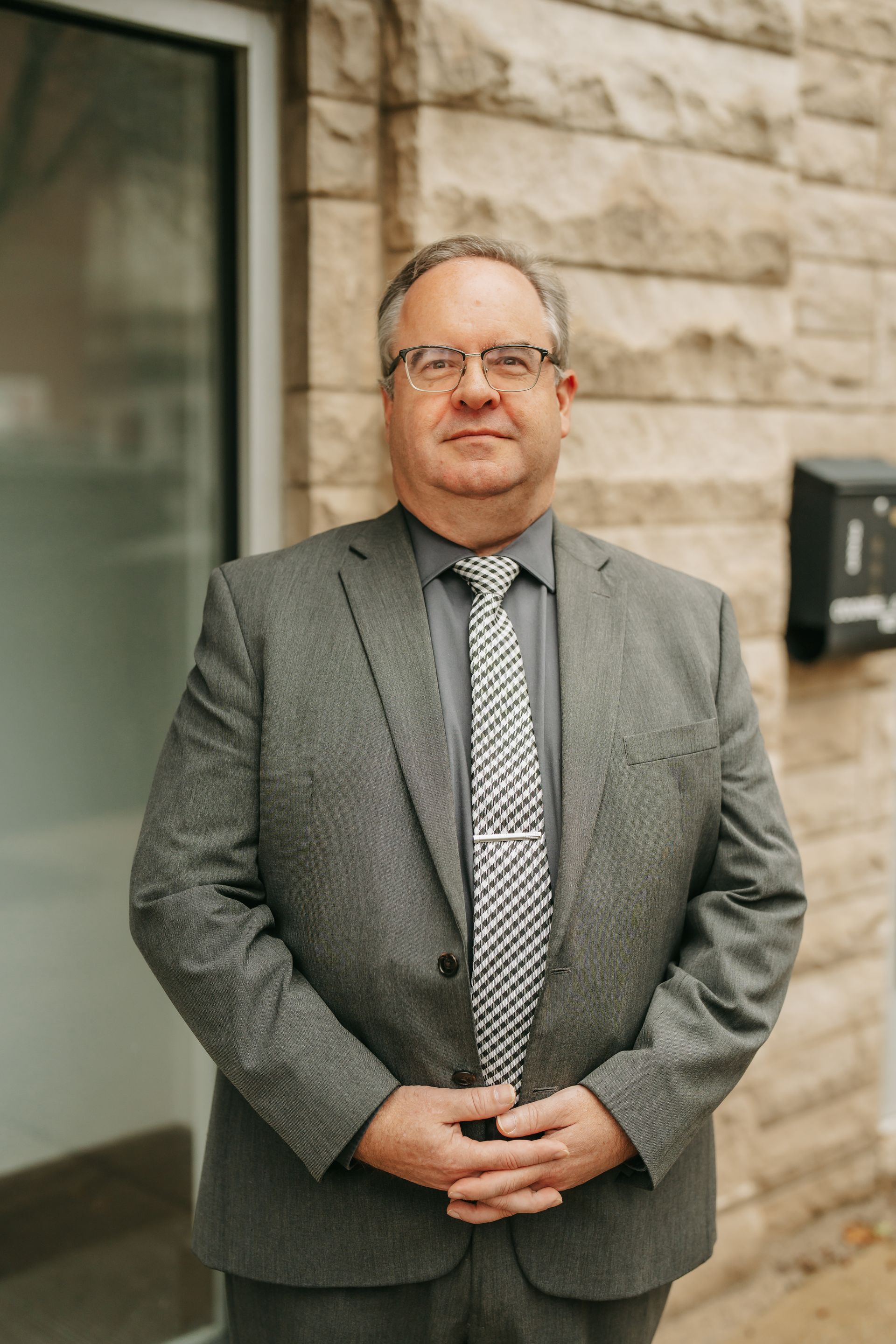 A man in a suit and tie is sitting down with his hands folded.