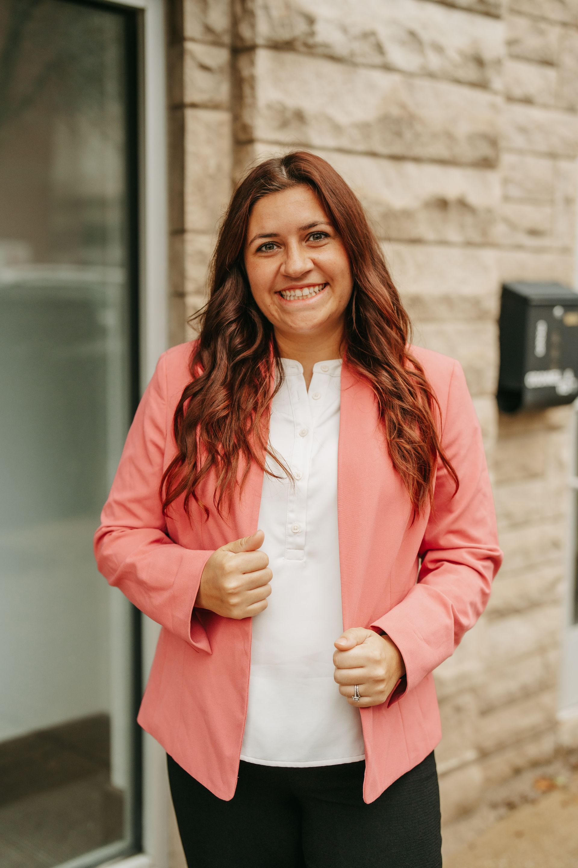 The woman is wearing a purple jacket and smiling with her arms crossed.