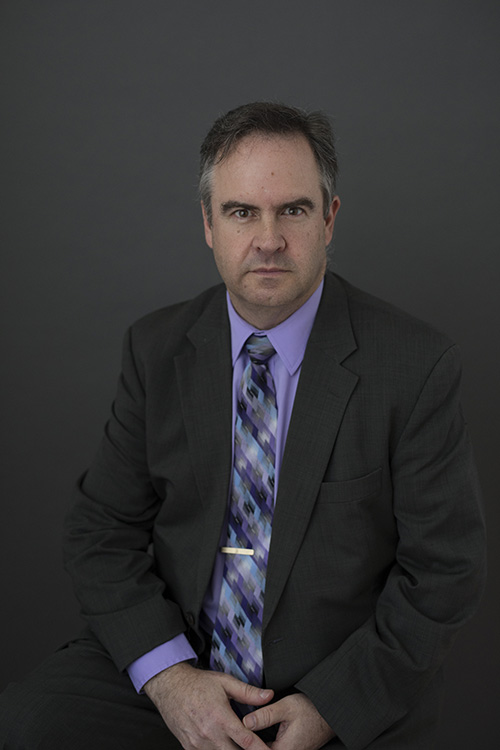 A man in a suit and tie is sitting down with his hands folded.