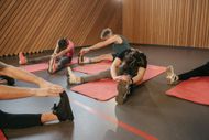 A group of people are stretching their legs on yoga mats in a gym.