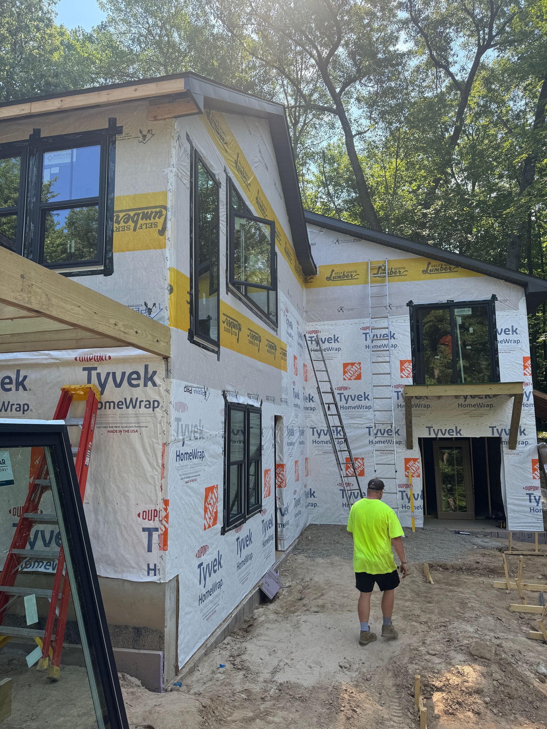 A man in a yellow shirt is walking in front of a house under construction.