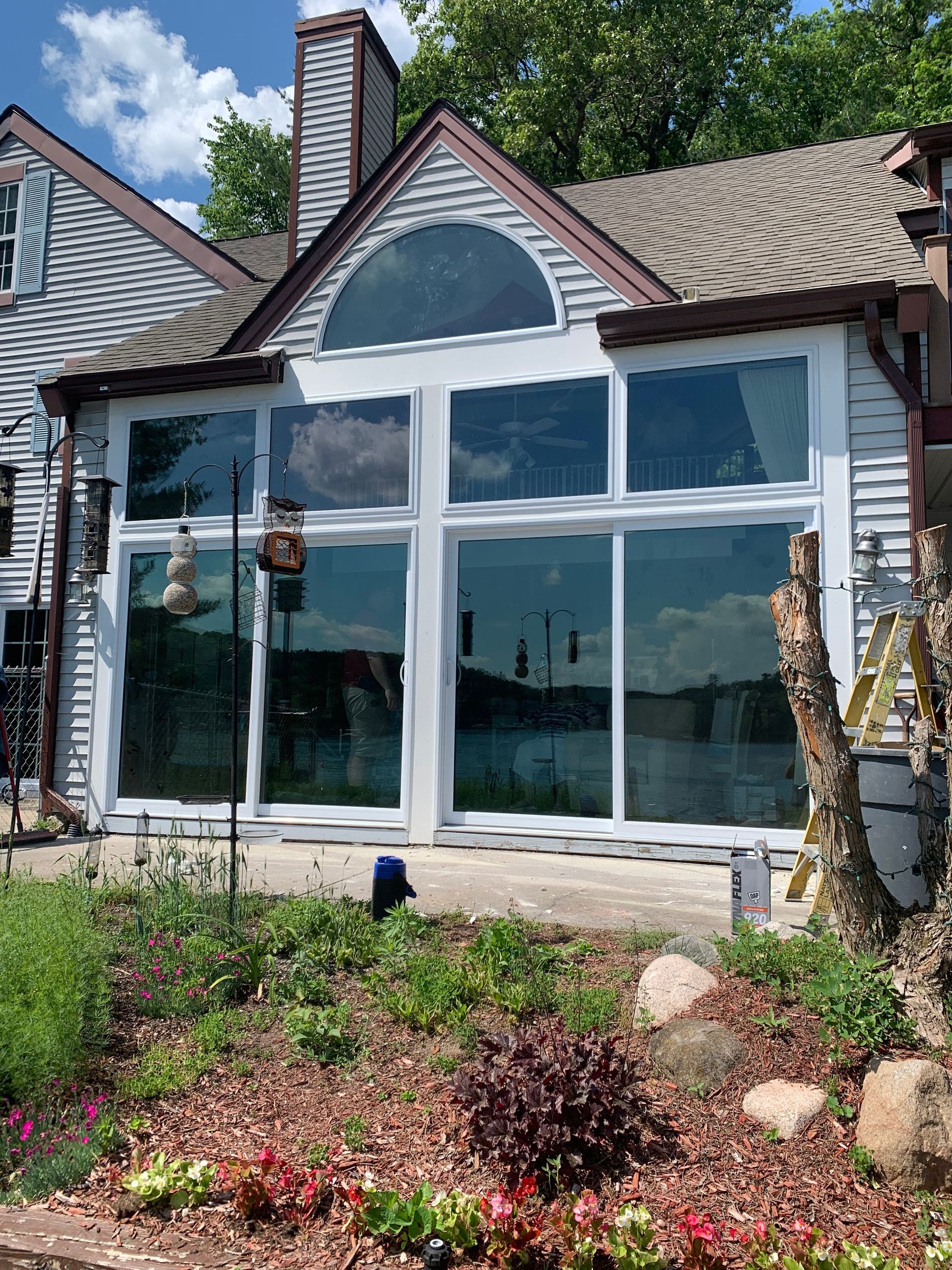 A house with a lot of windows and a lot of plants in front of it.