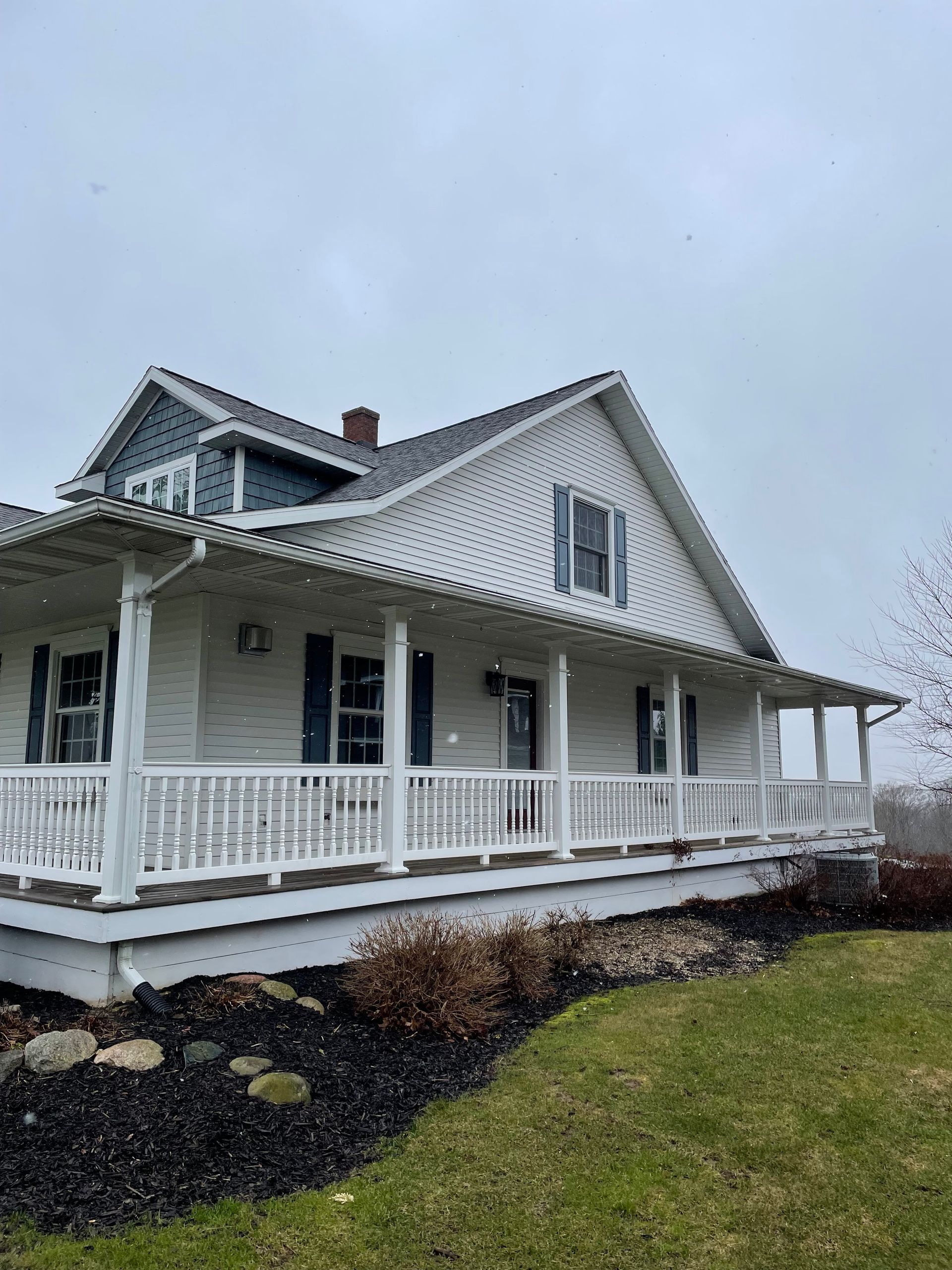 A white house with a large porch on a cloudy day.