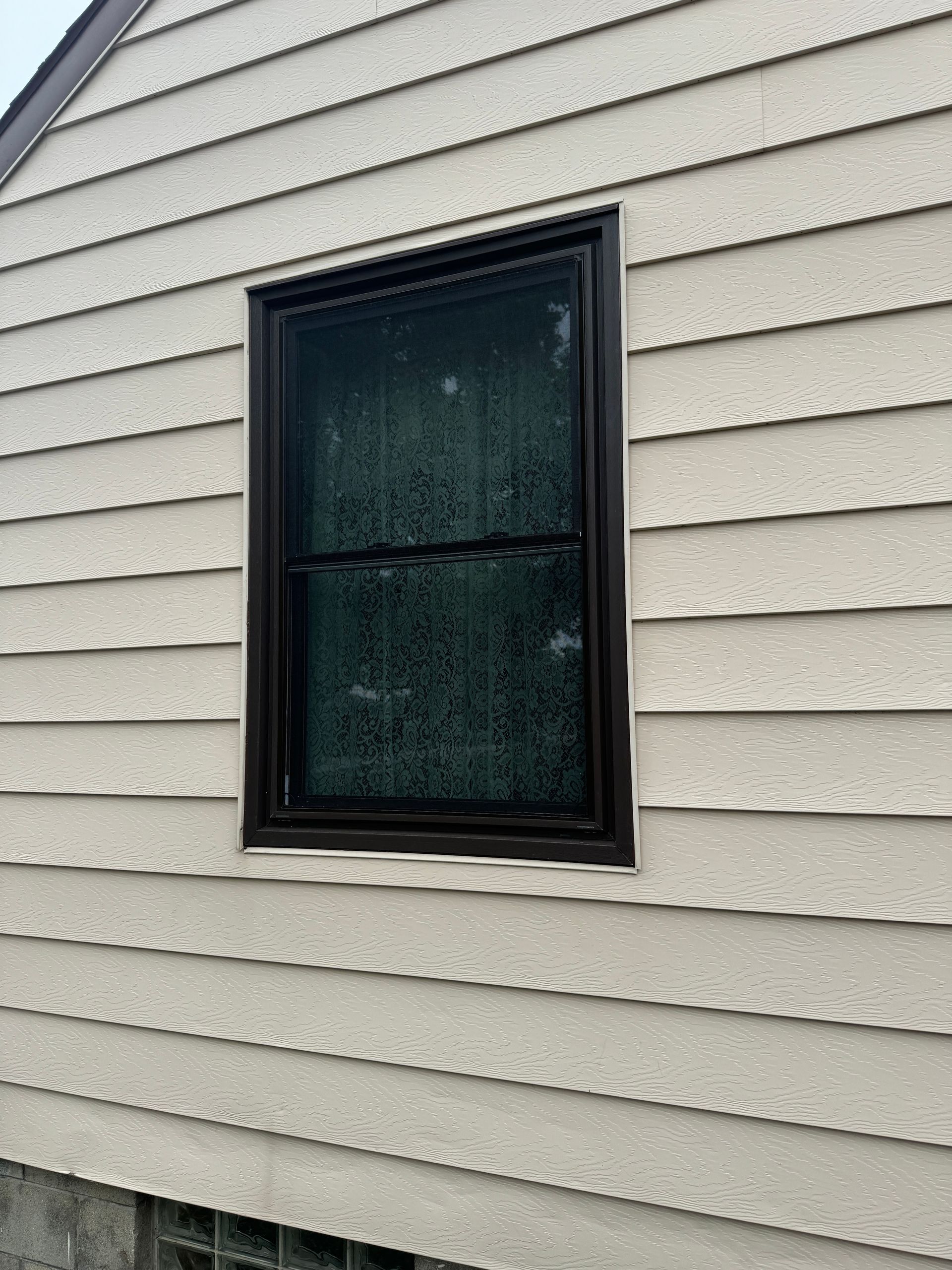A window on the side of a house with a brown frame.