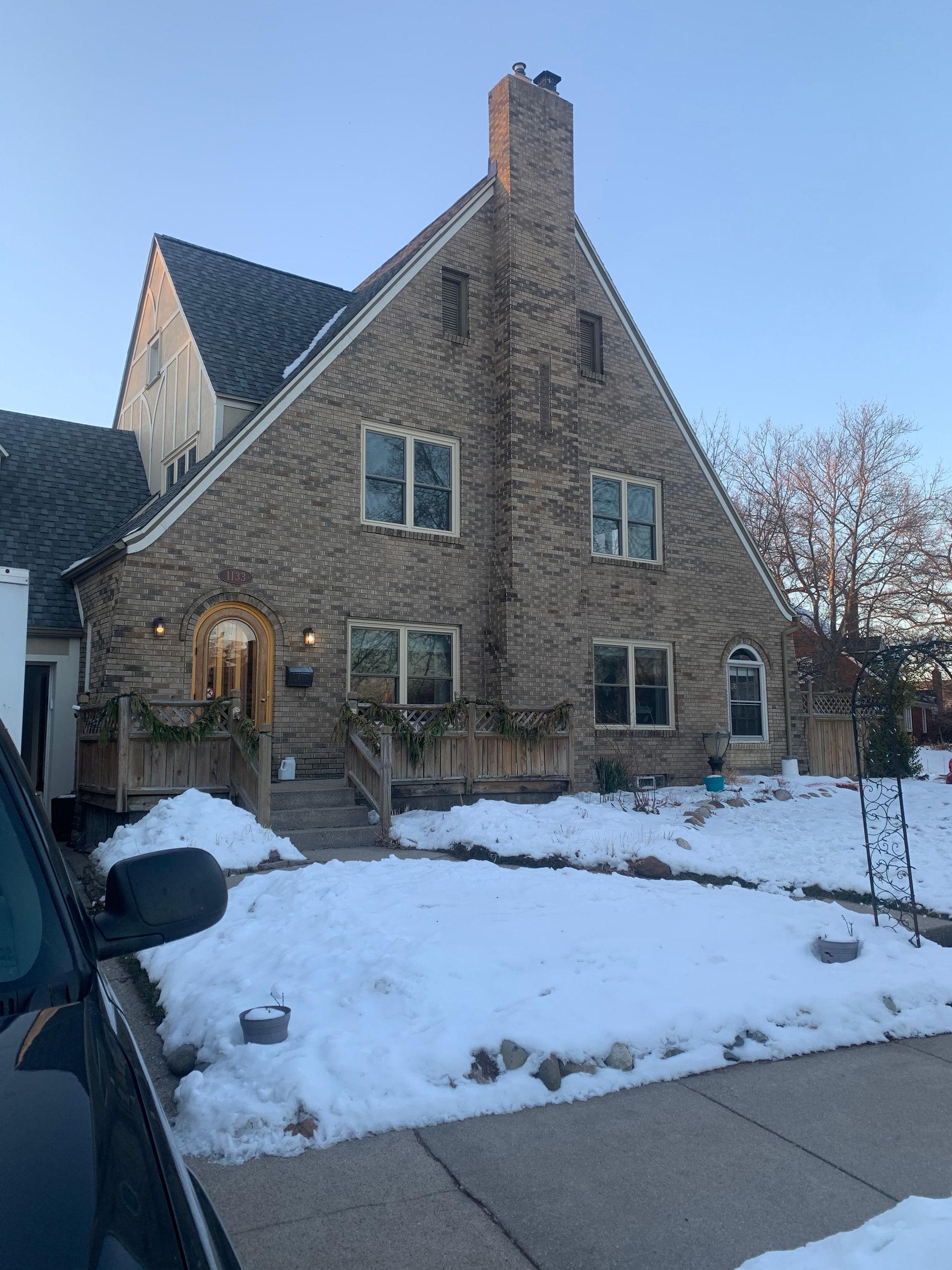 A large brick house with snow on the ground and a car parked in front of it.