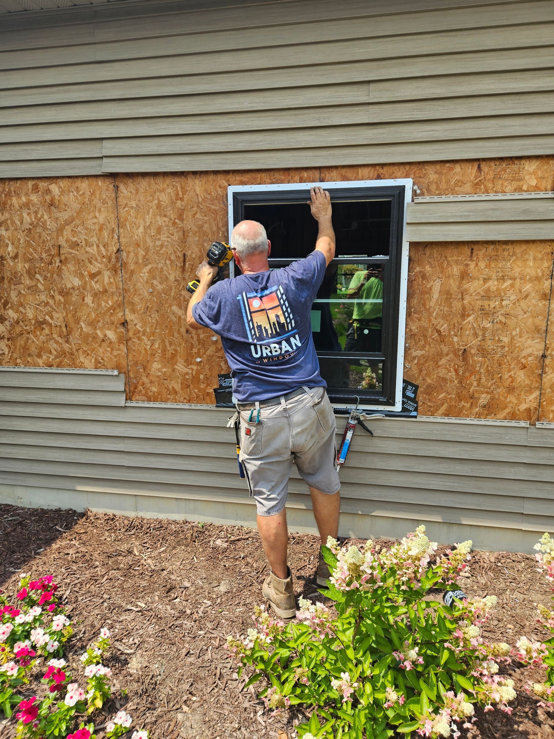 A man is installing a window on the side of a house.
