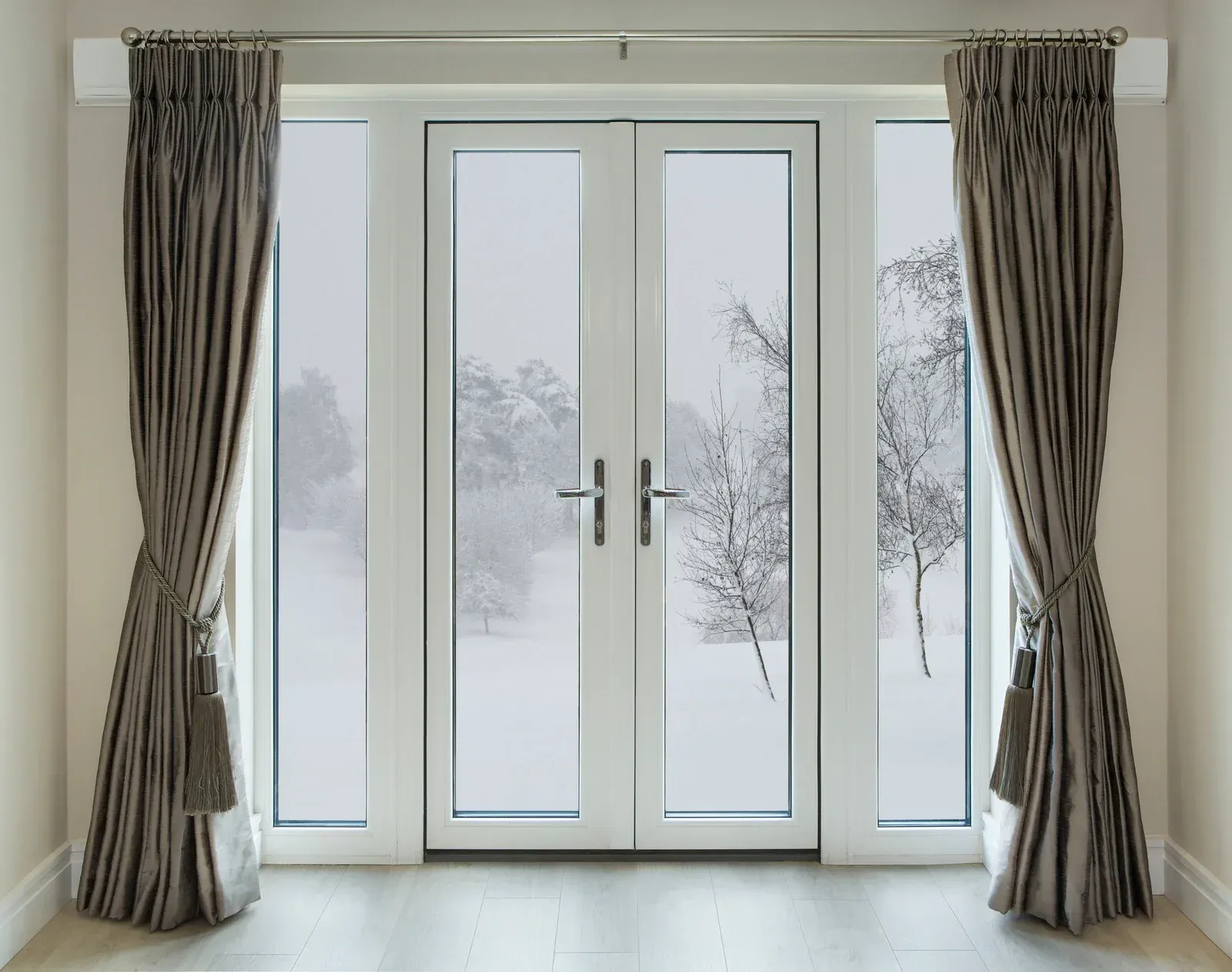 Gray curtains frame a white double door looking out at a snowy, winter landscape.