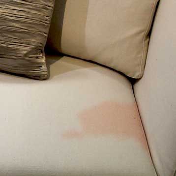 A white couch with a pillow and a stain on it.
