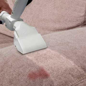 A person is cleaning a couch with a vacuum cleaner.