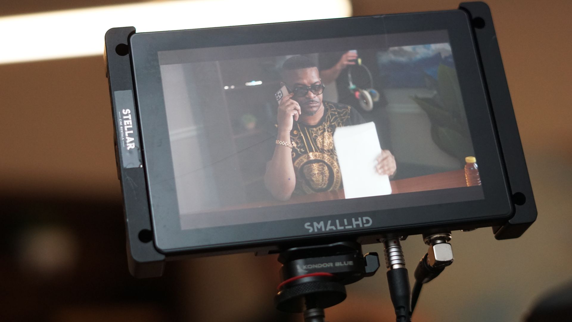 A man is holding a piece of paper in front of a small hd monitor.