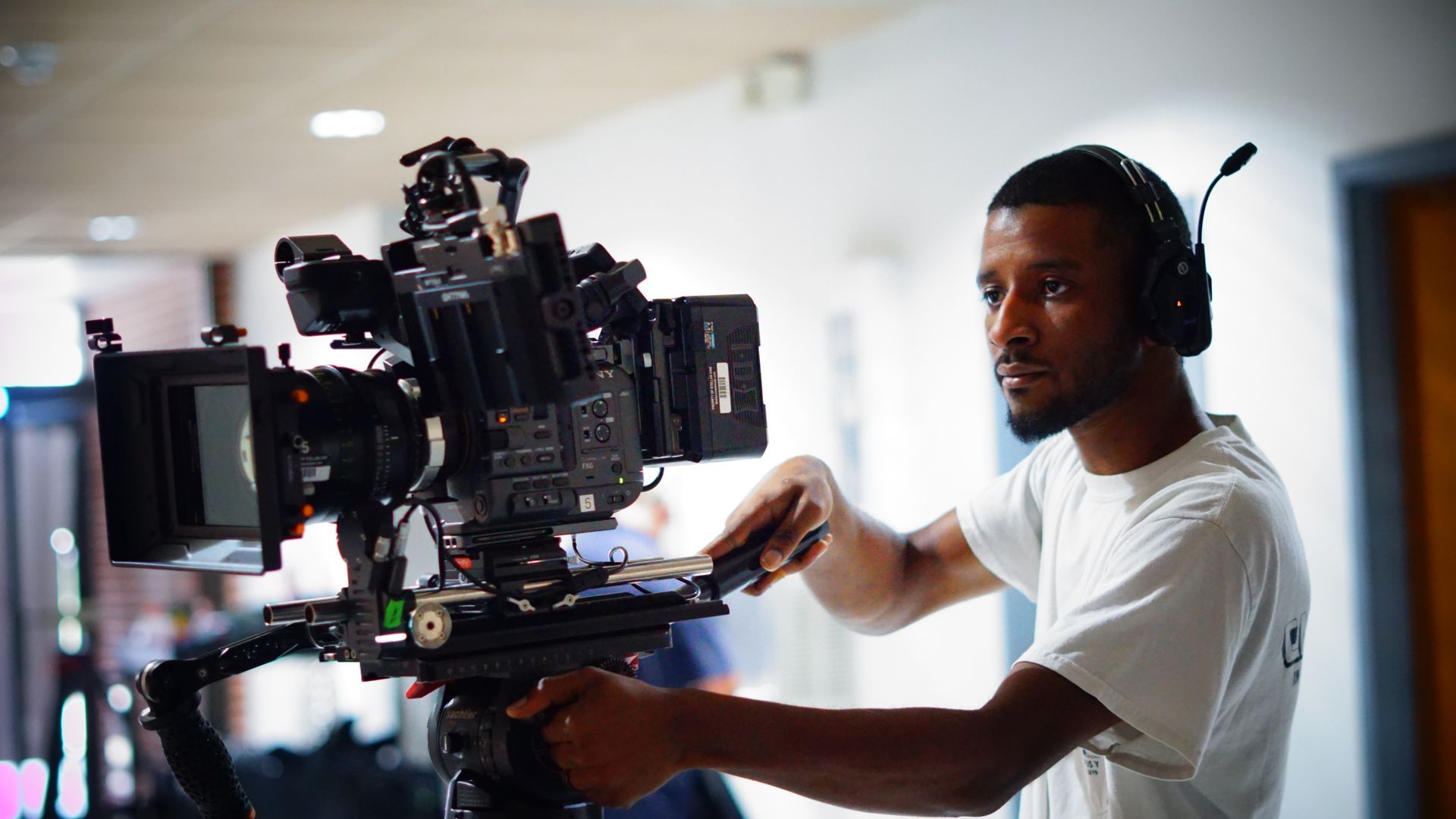 A man wearing headphones is working on a video camera.