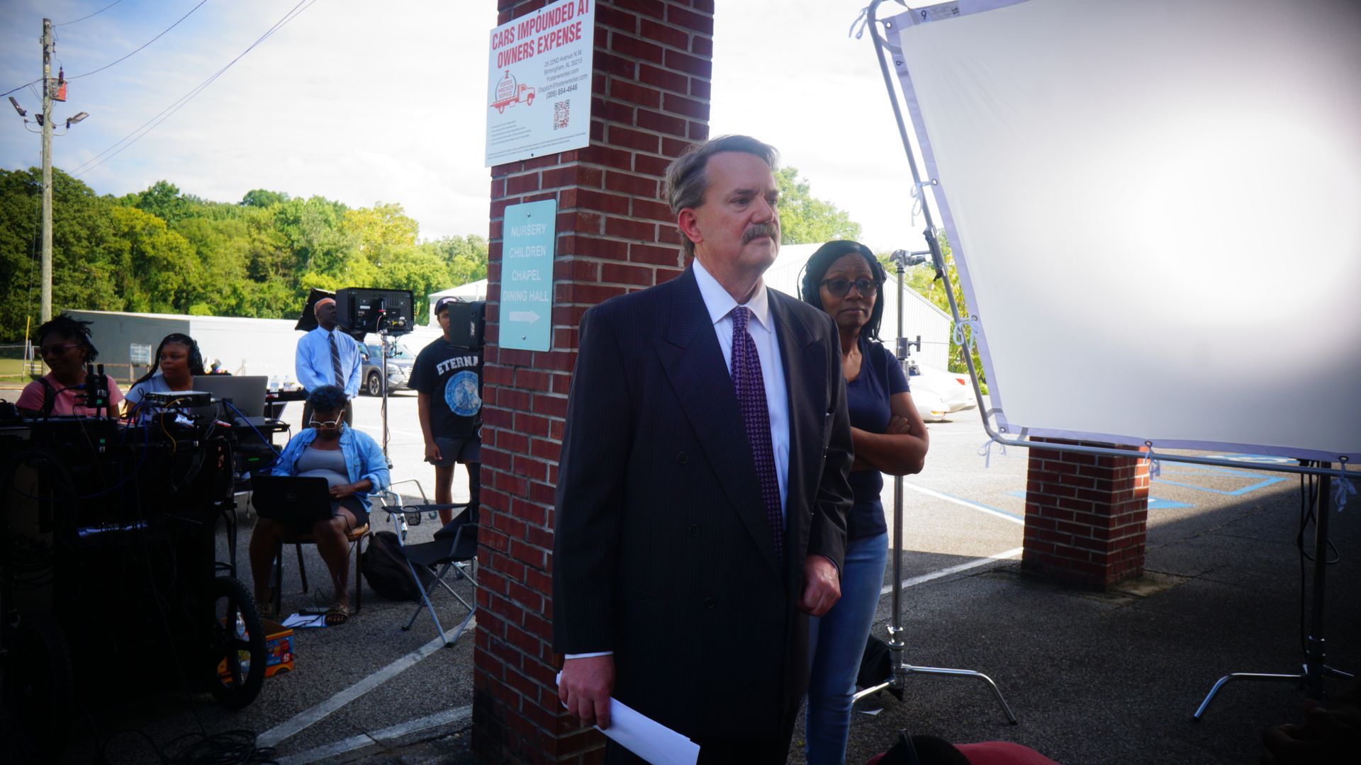 A man in a suit and tie is standing in front of a brick wall holding a piece of paper.