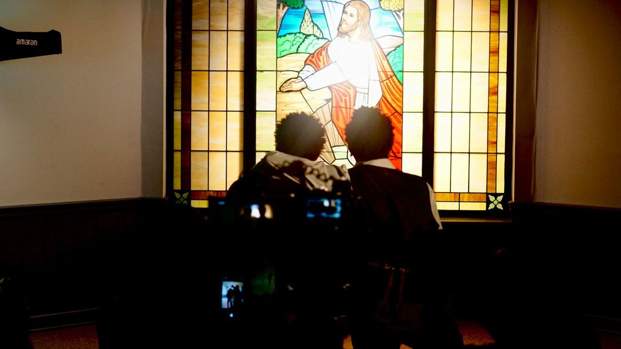 Two people are looking at a stained glass window of jesus.