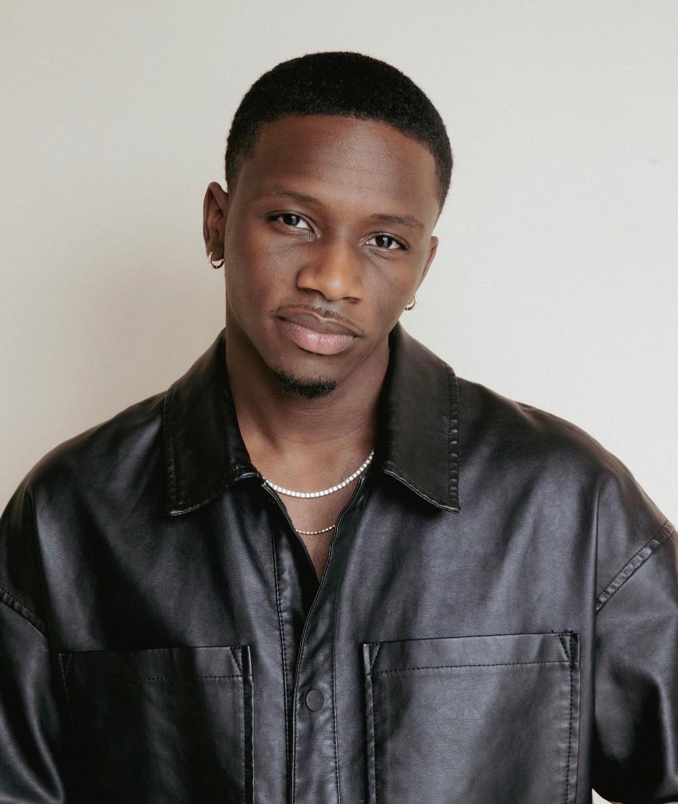 Person holds a film clapperboard, partially obscuring their face. They wear a black beanie and sweater; dark background.