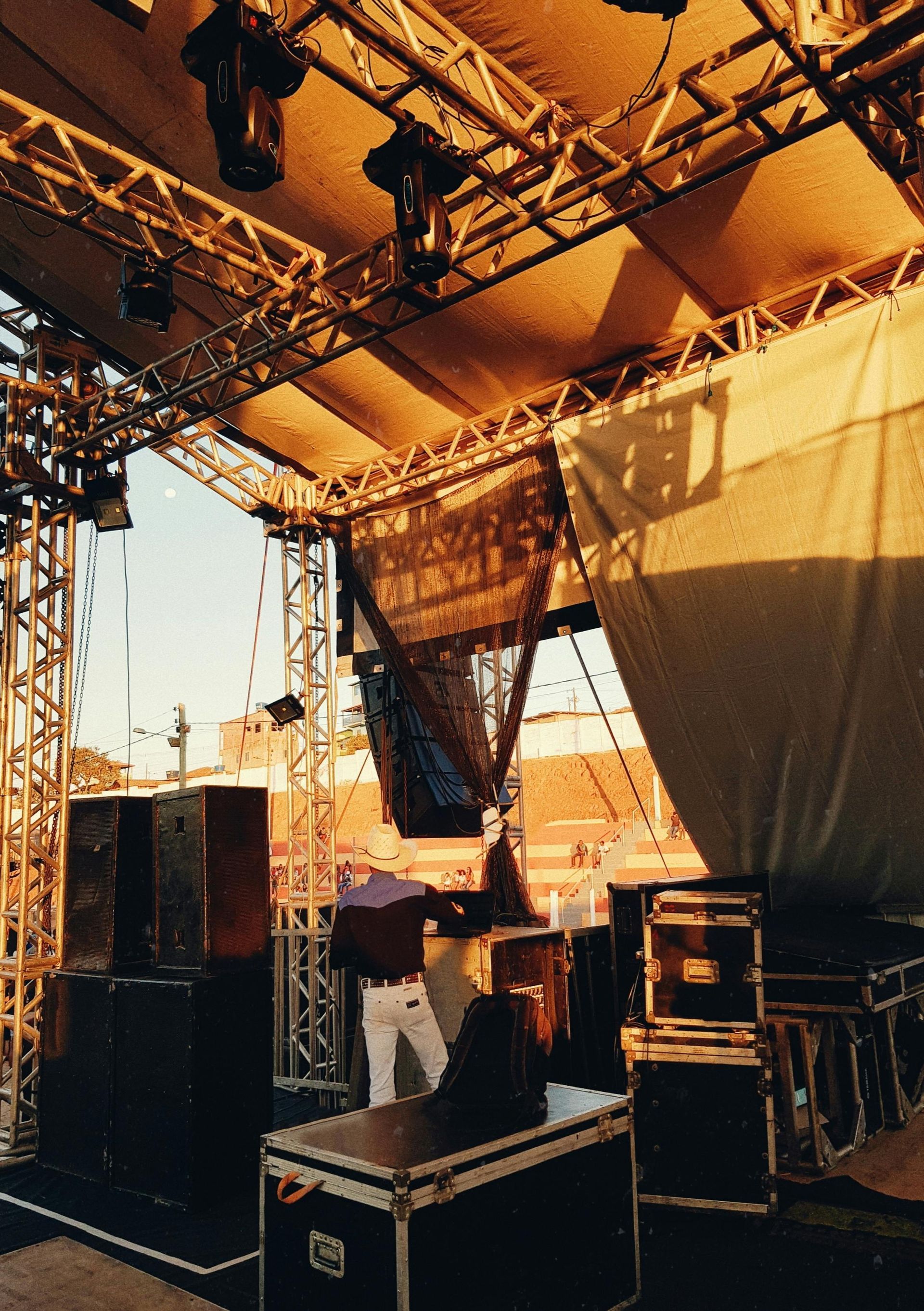 A stage set up outdoors with sound equipment, lighting, and a person near a sound board.