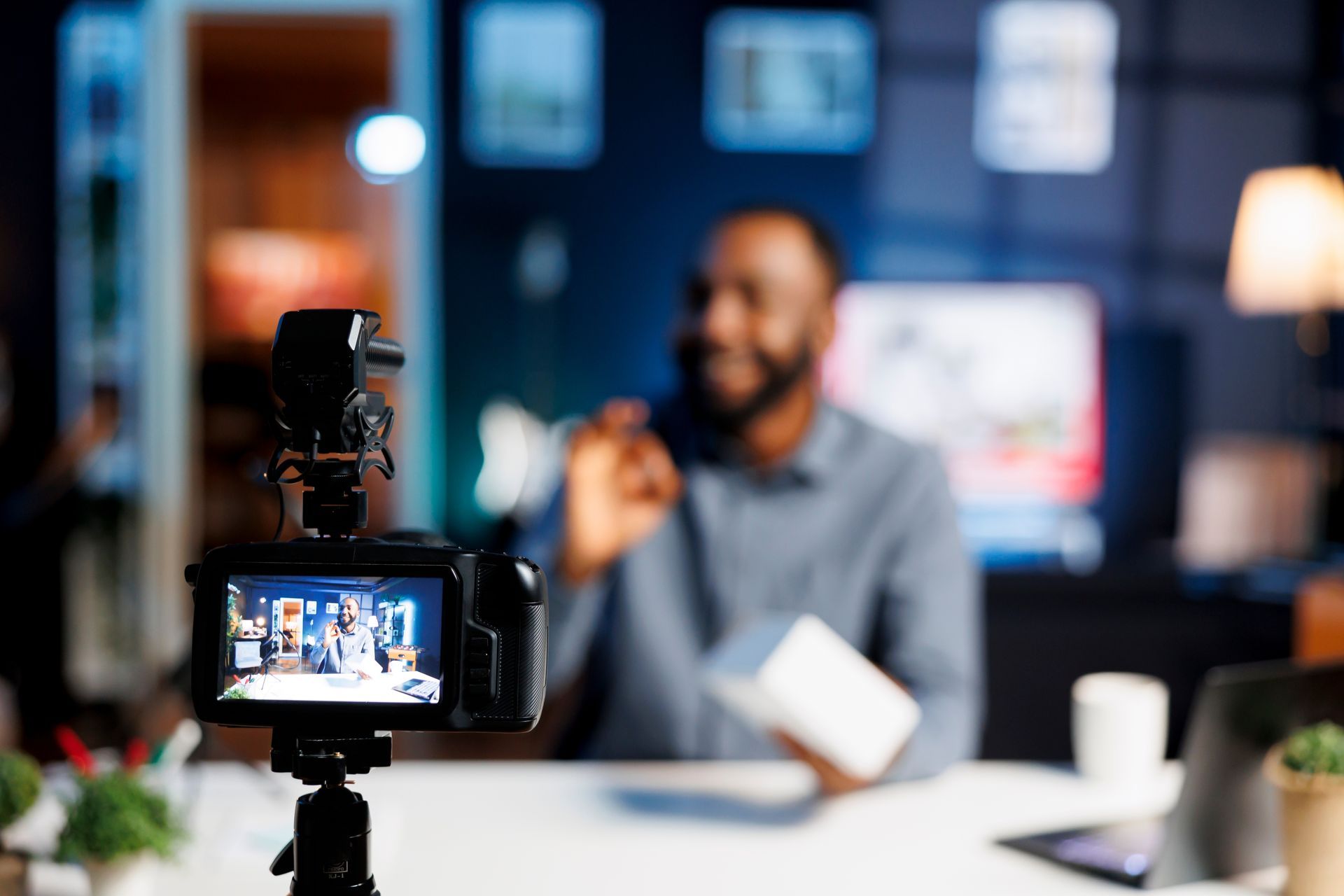 A man is sitting at a table being filmed by a camera.