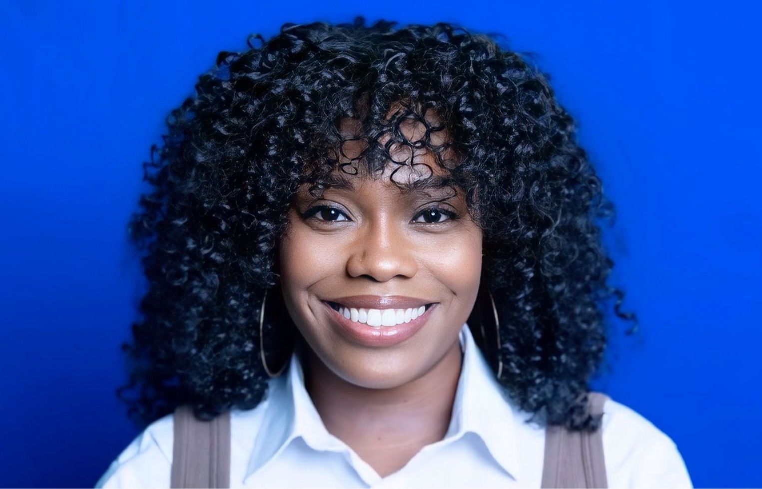 A woman with curly hair is smiling in front of a blue background.